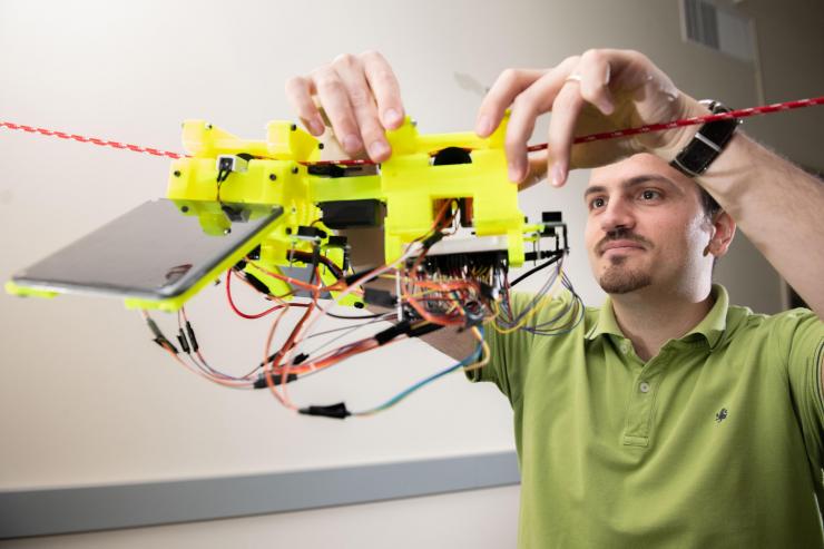 <p>Graduate Research Assistant Gennaro Notomista shows the components of SlothBot on a cable in a Georgia Tech lab. The robot is designed to be slow and energy efficient for applications such as environmental monitoring. (Photo: Allison Carter, Georgia Tech)</p>