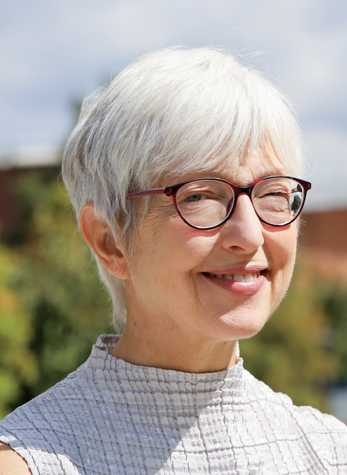 A headshot of a woman with cropped gray hair and glasses who is smiling at the camera