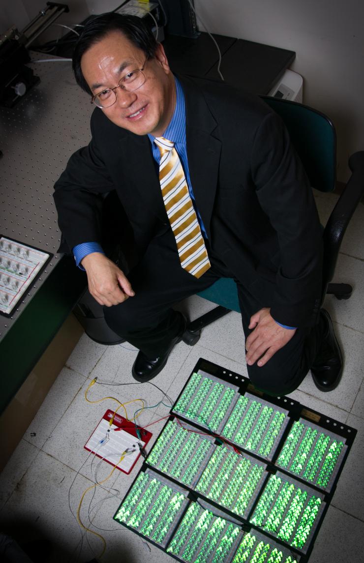 <p>Georgia Tech professor Zhong Lin Wang poses with an array of 1,000 LED lights that can be illuminated by power produced by the force of a shoe striking a triboelectric generator placed on the floor. (Credit: Rob Felt, Georgia Tech).</p>