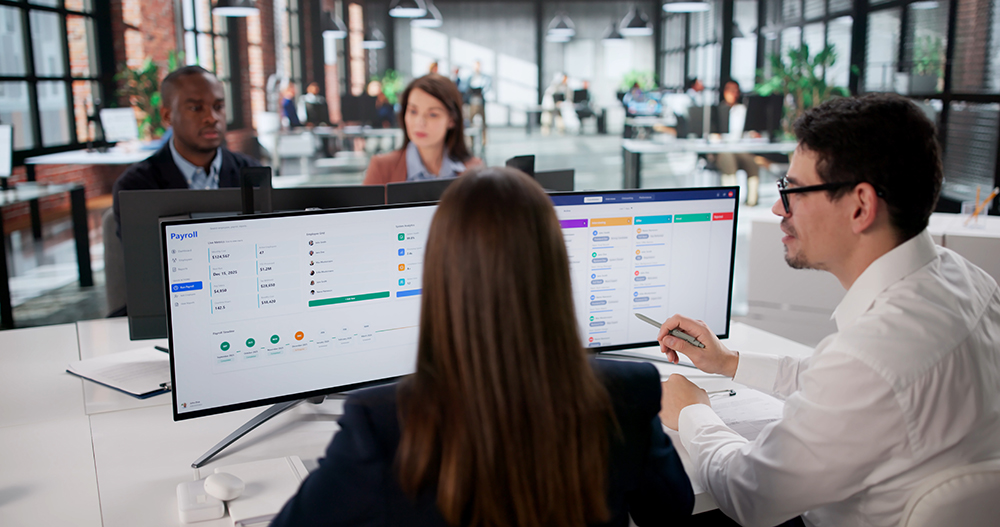 Staff members collaborating in an office while reviewing funding and project management information on a computer dashboard.