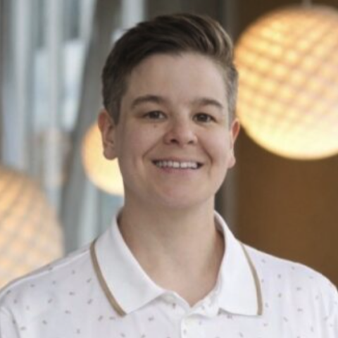 A woman with short brown hair wearing a white collared shirt smiles for a photo with hanging light fixtures in the background.