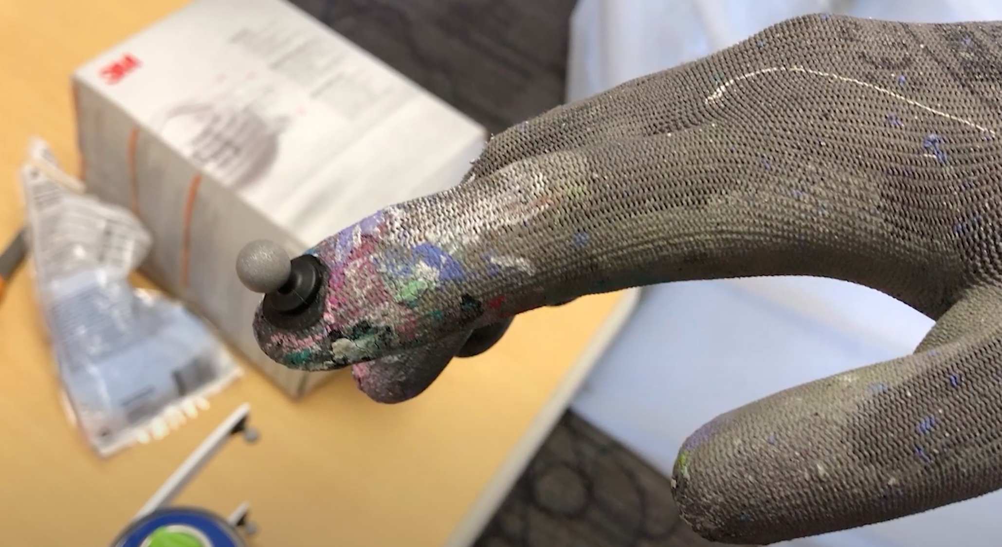 A glove with paint on it has a sensor on the fingertip that looks like a black and grey bulb.