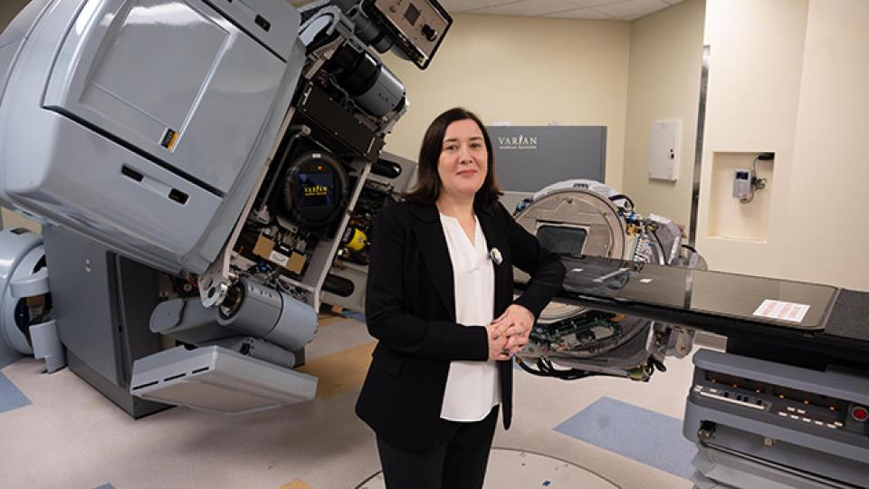 Person standing in a medical treatment room with advanced radiotherapy equipment, including a large Varian machine and treatment table.