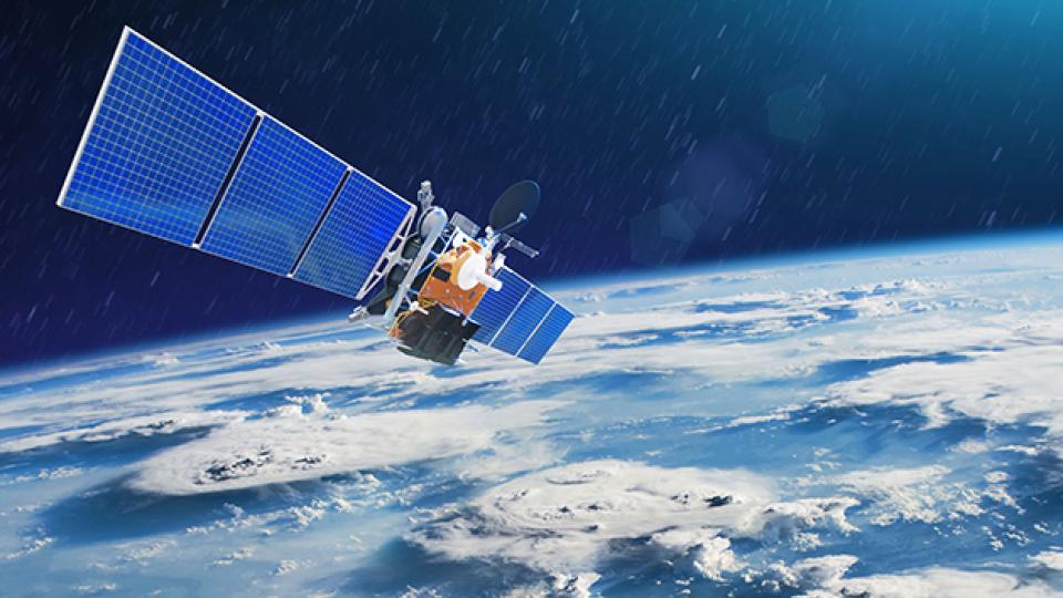 Satellite with large blue solar panels orbiting above Earth, showing cloud formations and the planet's curvature against a dark space background