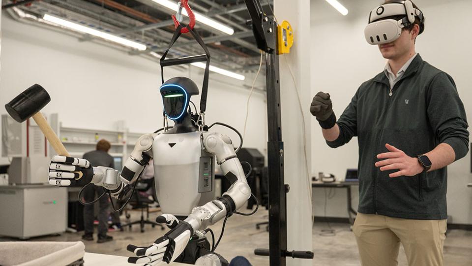Person wearing a virtual reality headset controlling a humanoid robot equipped with tools in a laboratory setting.