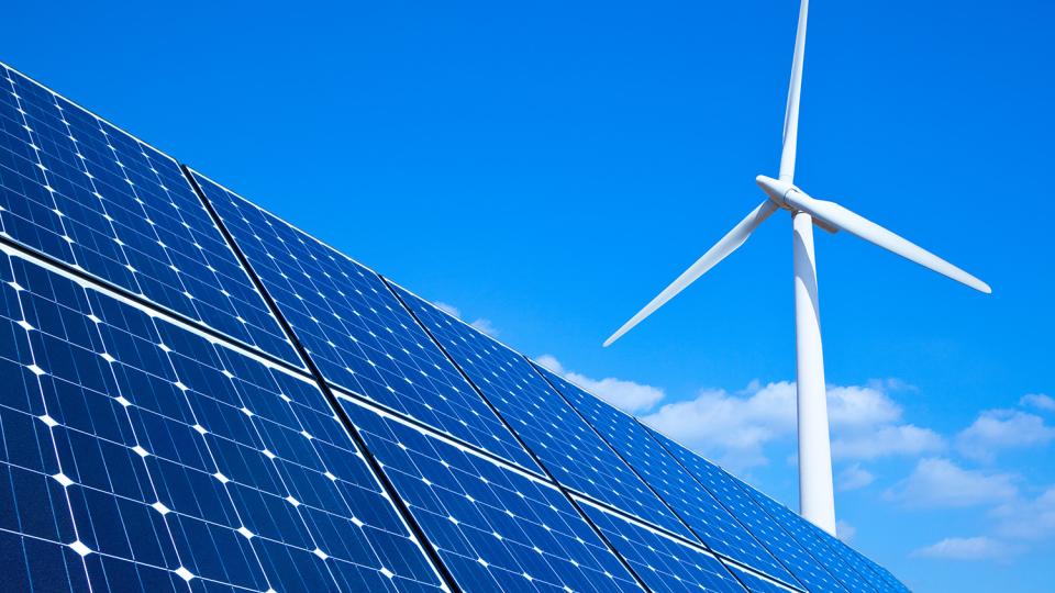Solar panels cut across the foreground of an image featuring a blue sky and a white wind turbine