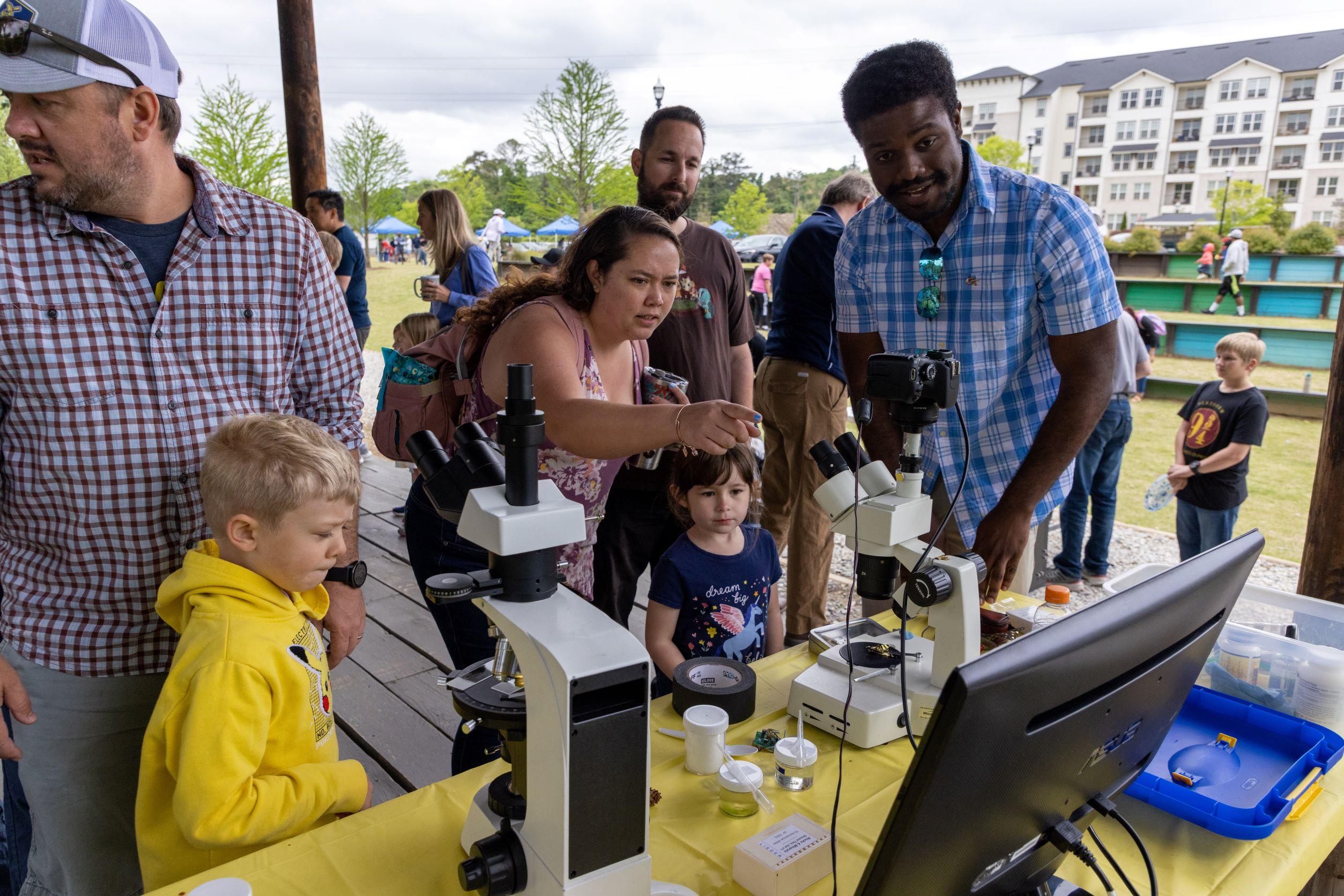A group looking through microscopes set up by GTRI volunteers at the Science Day in the Park (Photo Credit: Ethan Trewhitt). 