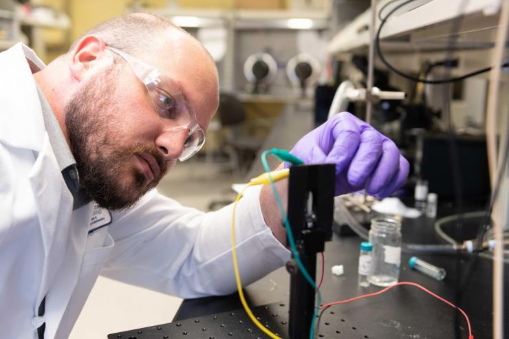 <p>Graduate Research Assistant Dylan Christiansen studies the electrochromic properties of new materials in a transparent electrochemical cell that allows examination of color change upon application of an oxidizing voltage. (Photo: Allison Carter, Georgia Tech)</p>