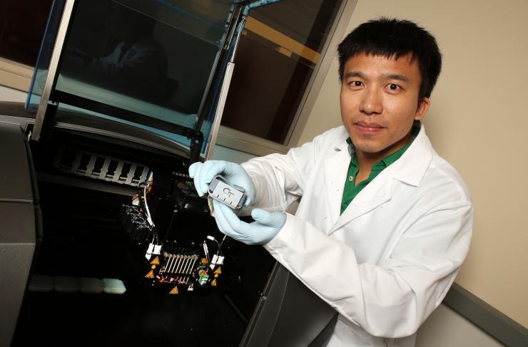 <p>Yiqi Mao, a postdoctoral fellow in the laboratory of Professor Jerry Qi at Georgia Tech, shows a folded box structure produced from smart shape-memory materials. The materials were created with the 3-D printer shown with him. (Credit: Candler Hobbs, Georgia Tech)</p>