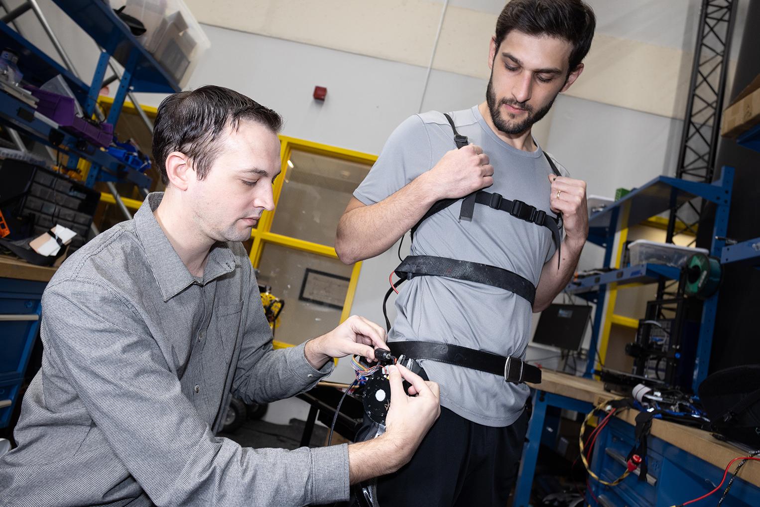 Researcher Aaron Young makes adjustments to an experimental exoskeleton worn by then-Ph.D. student Dean Molinaro.