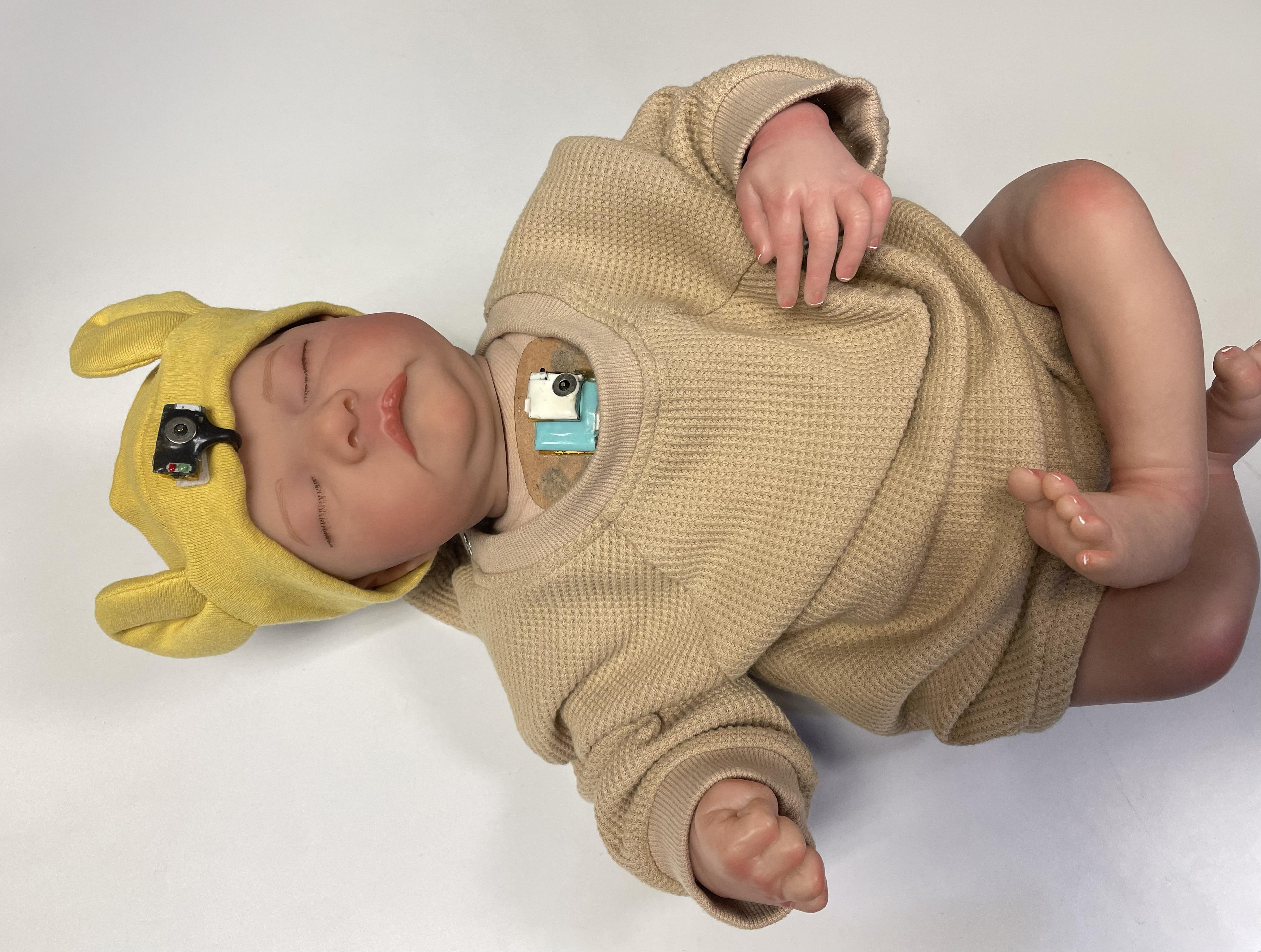 Wearable chest-mounted patch and forehead-mounted pulse oximeter shown on a mannequin baby for illustration