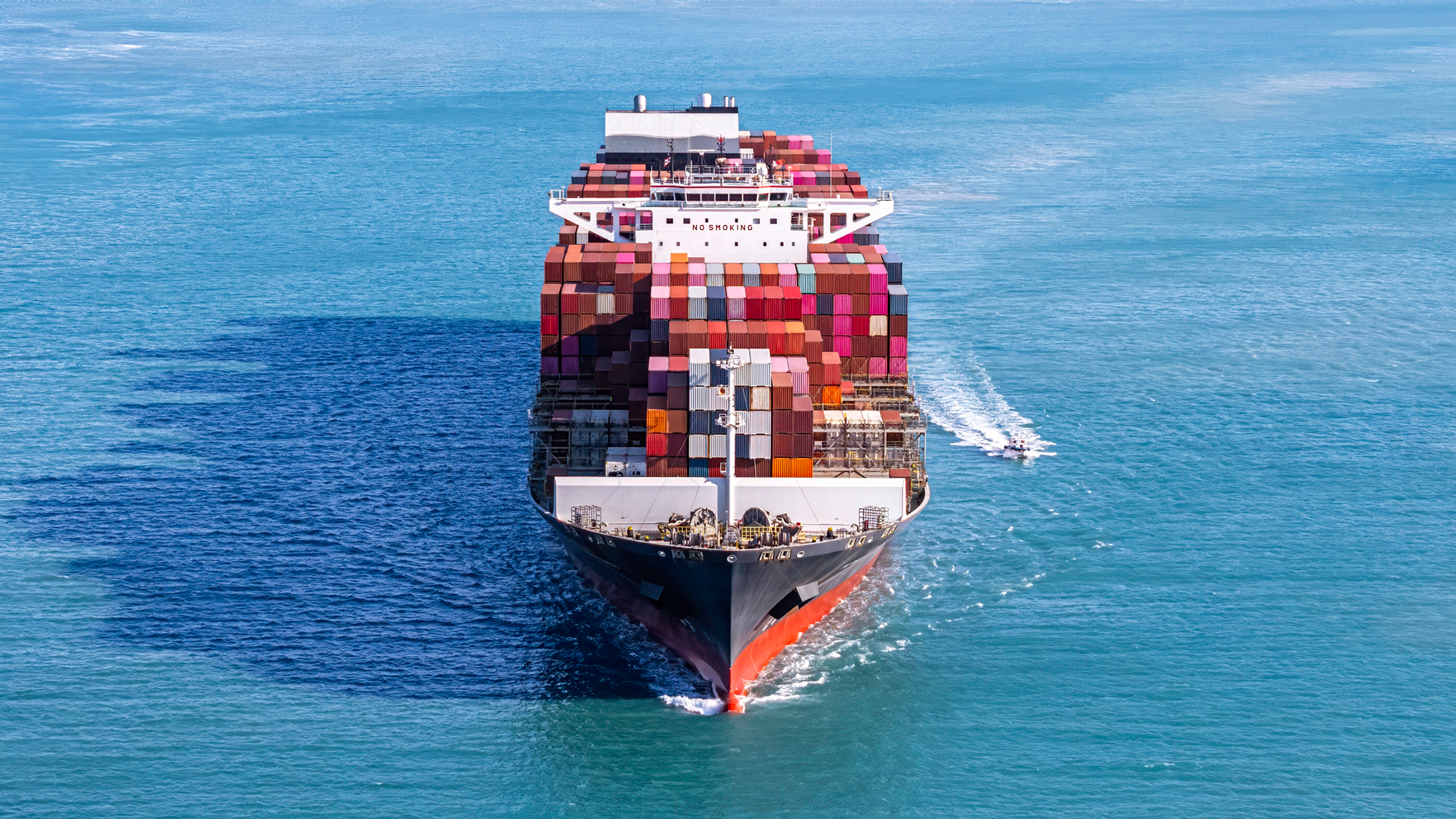 A cargo ship filled to the brim with colorful containers sails across a blue ocean