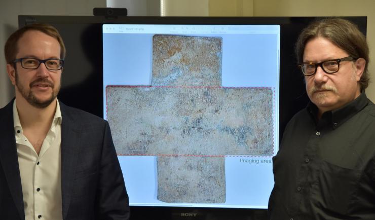 <p>Georgia Tech professor David Citrin (right) and adjunct professor Alexandre Locquet stand in front of an image of the 16th-century funerary cross used in their study. Credit: Nicolas Jacquet</p>
