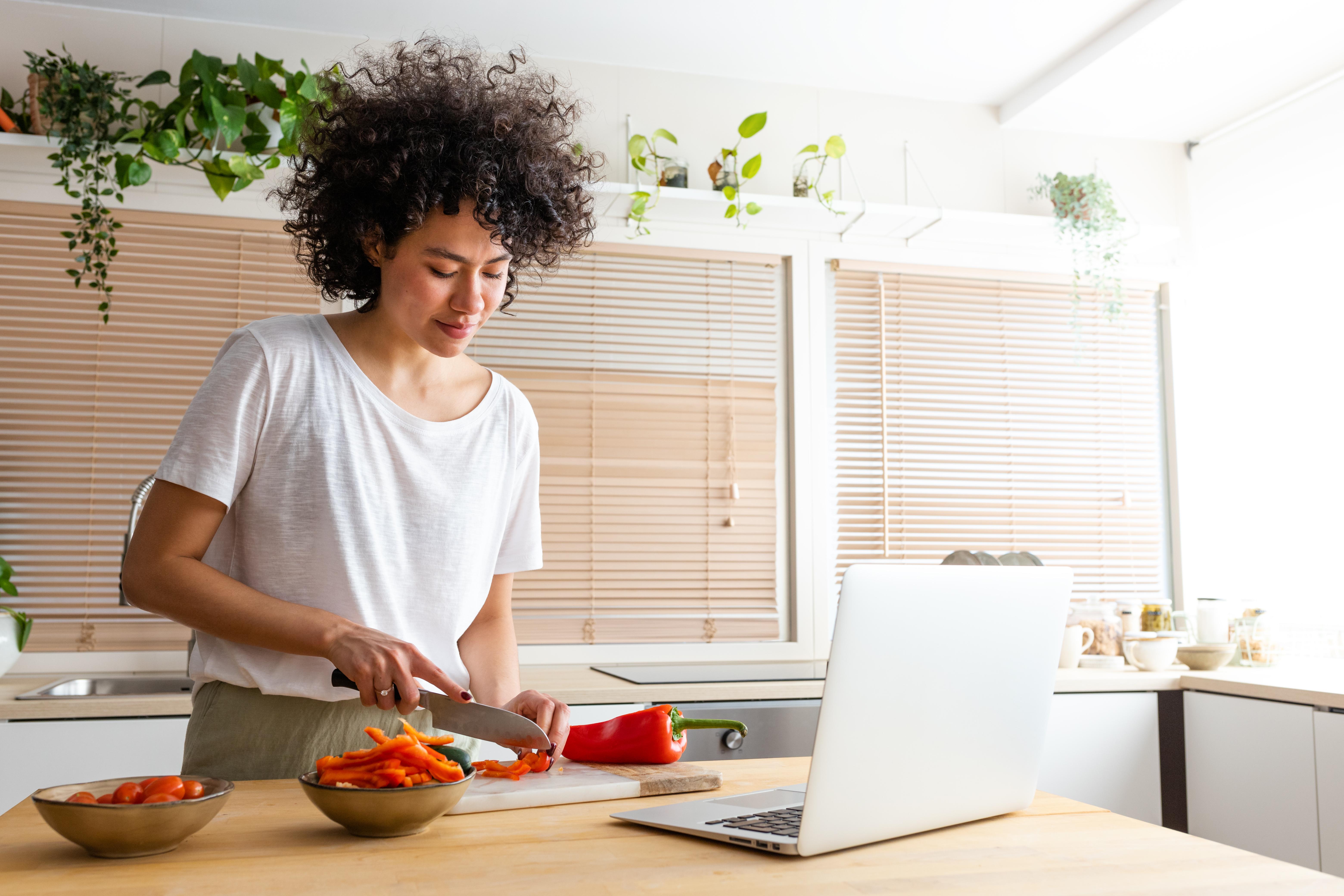 Woman chopping peppers in front of laptop