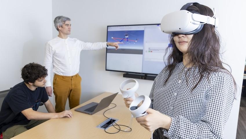 A female student wears the Meta Quest VR headset with two men standing behind her