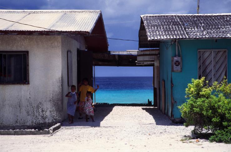 <p>Children are shown with buildings in Majuro, the Marshall Islands, with the sea nearby. The Marshall Islands are facing effects of climate change as sea levels rise. (Credit: Wikimedia Commons)</p>