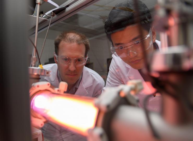 <p>Georgia Tech Professor Lukas Graber and Postdoctoral Fellow Chanyeop Park study the plasma potential surrounding materials being evaluated for use in improved DC circuit breakers. The low-energy argon plasma creates the purple color. (Photo: Rob Felt, Georgia Tech)</p>