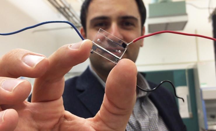 <p>Fatih Sarioglu, an assistant professor in Georgia Tech’s School of Electrical and Computer Engineering, holds a hybrid microfluidic chip that uses a simple circuit pattern to assign a unique seven-bit digital identification number to each cell passing through the channels. (Credit: John Toon, Georgia Tech)</p>