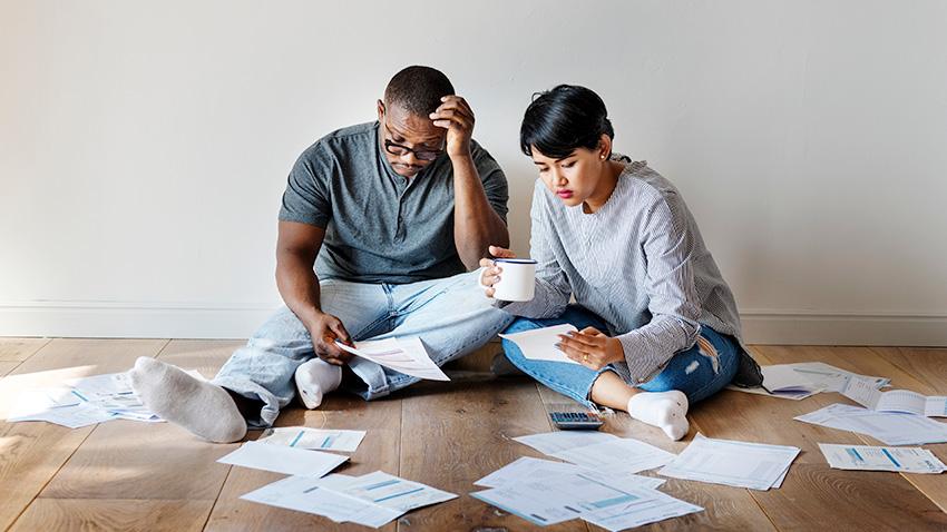Stock image of young couple looking troubled with bills spread across the wooden floor