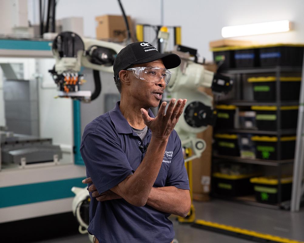 A man wearing a cap, safety goggles, and a navy shirt speaks in an industrial setting.