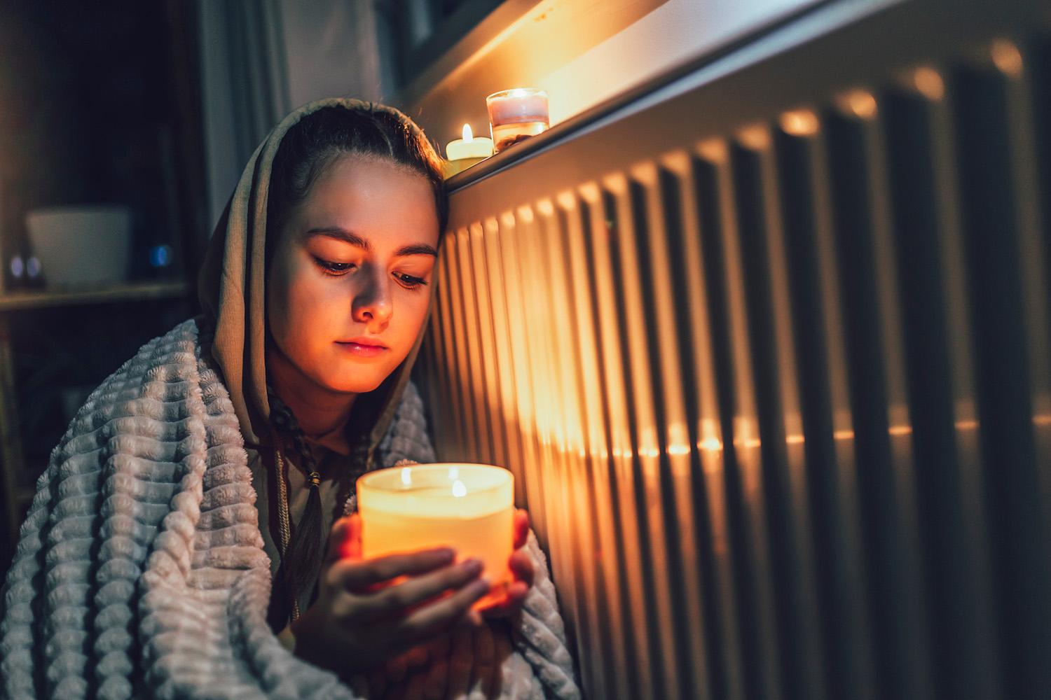 A young girl wrapped in a blanket holds a candle during a power outage.