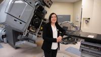 Person standing in a medical treatment room with advanced radiotherapy equipment, including a large Varian machine and treatment table.