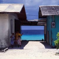Children are shown with buildings in Majuro, the Marshall Islands, with the sea nearby. The Marshall Islands are facing effects of climate change as sea levels rise. (Credit: Wikimedia Commons)