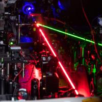A red laser creates nonlinear effects with tiny triangles of gold. The blue beam shows the frequency-doubled light and the green beam controls the hot-electron migration. (Credit: Rob Felt, Georgia Tech)