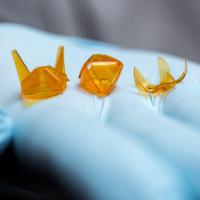 A new technique for producing self-folding three-dimensional origami structures from photo-curable liquid polymer materials created these tiny samples, held in a hand for size comparison. (Credit: Rob Felt, Georgia Tech)