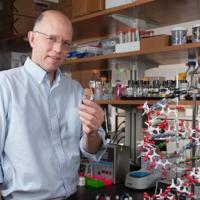 <p>Professor Nicholas Hud holds a vial containing synthesized molecules that spontaneously assemble into structures that resemble the helical structure of DNA (model in foreground).</p>