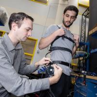 two people in the lab make adjustments to a robotic exoskeleton