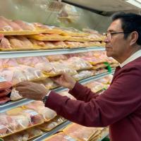A man in a crimson colored sweater peruses the meat cooler in a supermarket.