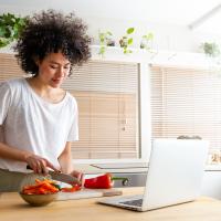 Woman chopping peppers in front of laptop