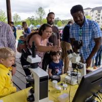 <p><em>A group looking through microscopes set up by GTRI volunteers at the Science Day in the Park (Photo Credit: Ethan Trewhitt). </em></p>