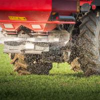 Closeup view of a red tractor spreading fertilizer pellets in a field.
