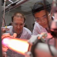 <p>Georgia Tech Professor Lukas Graber and Postdoctoral Fellow Chanyeop Park study the plasma potential surrounding materials being evaluated for use in improved DC circuit breakers. The low-energy argon plasma creates the purple color. (Photo: Rob Felt, Georgia Tech)</p>