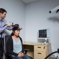 <p>Researcher Dobromir Rahnev demonstrates the application of transcranial magnetic stimulation (TMS) in a Georgia Tech psychology research center with graduate student Ji-Won Jung. Credit: Georgia Tech / Rob Felt</p>