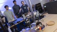 Three men use their phones to control a robot arm