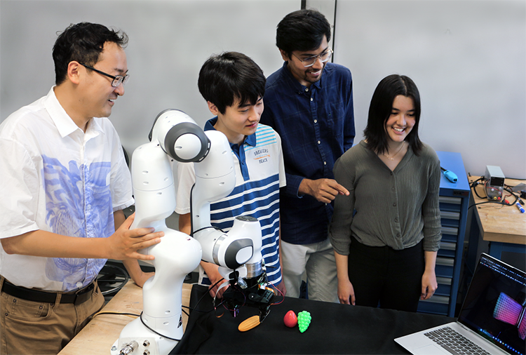 Professor Ye Zhao (GT-ME), high school intern Matthew Zhu, graduate student Chaitanya Mehta, and high school intern Christian Hable with the lab's robotic arm with tactile sensors. - Image Credit: Christa M. Ernst